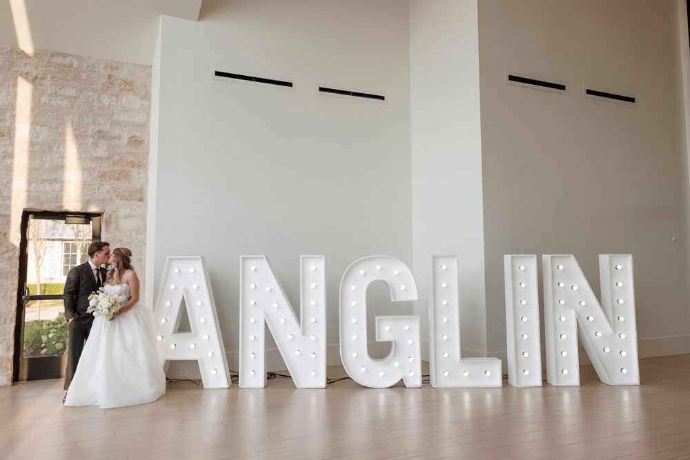Large white letters spelling 'DANGLIN' mounted on a white wall in a gallery-style space with brick elements.