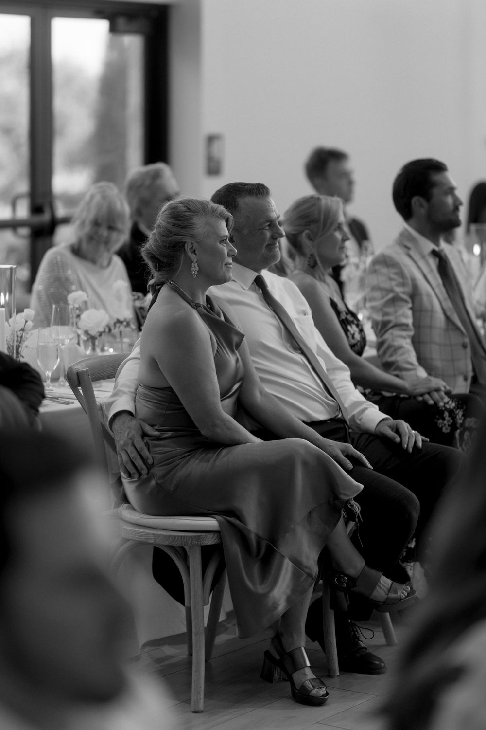 Black and white photo of people sitting in rows of chairs at an indoor gathering or presentation.