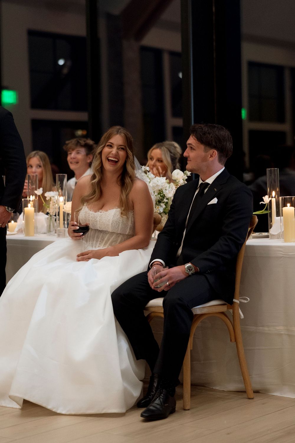 A newlywed couple shares a joyful moment during their wedding reception, seated together at an elegantly decorated table.
