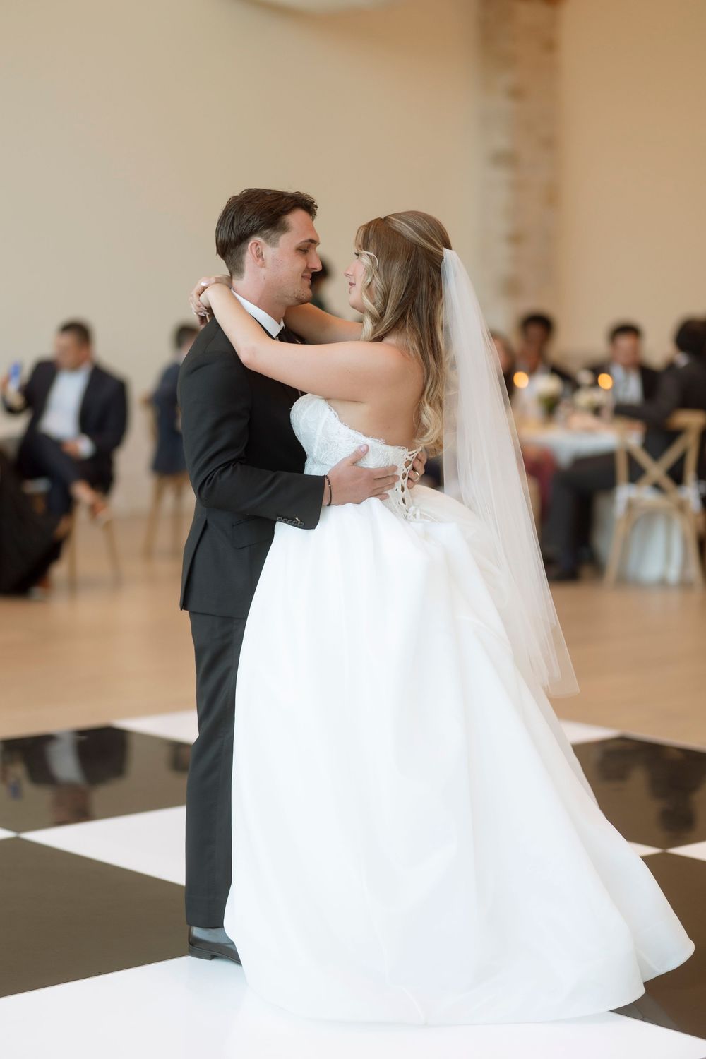 A bride and groom share their first dance at their wedding reception on a white dance floor in an elegant ballroom.