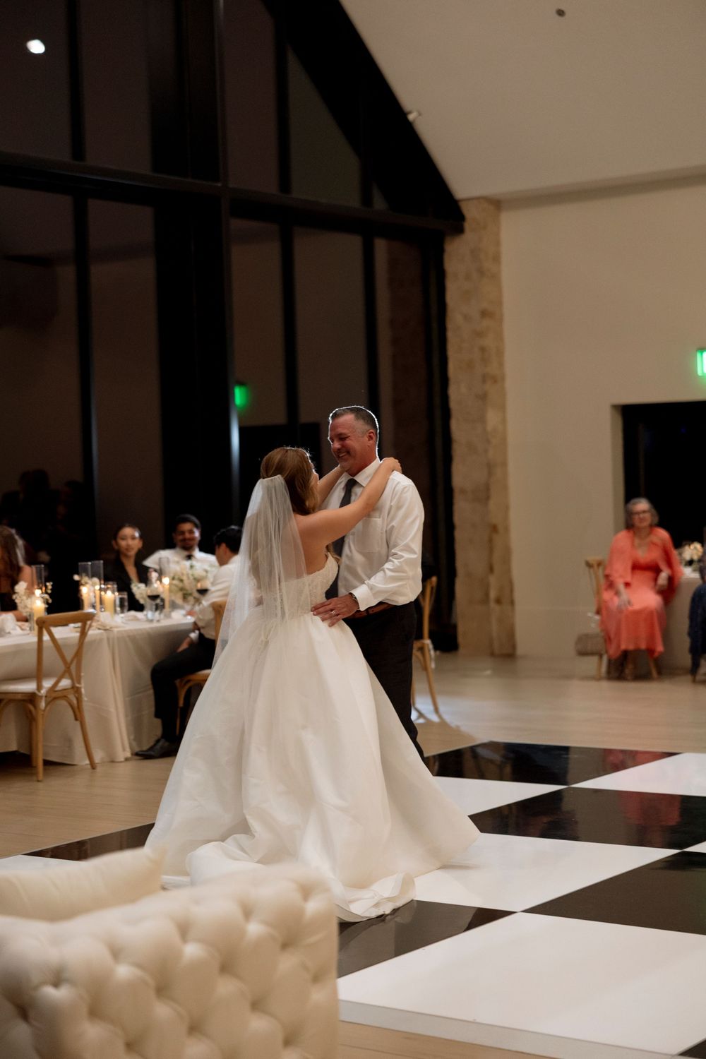 A couple shares their first dance as newlyweds on a black and white checkered dance floor at an elegant reception venue.