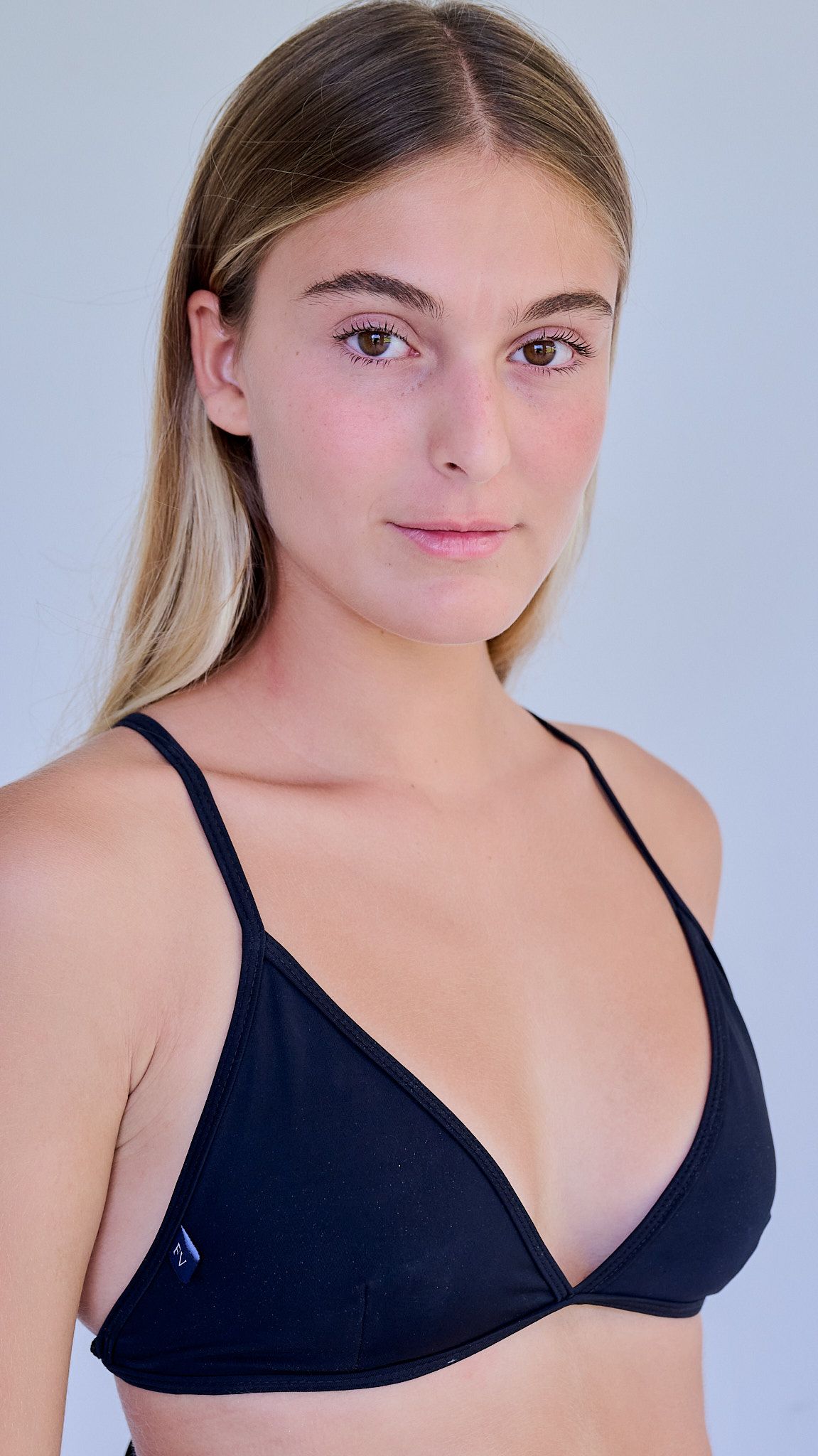 Model wearing a white crop top and light blue high-waisted jeans poses against a light blue background.
