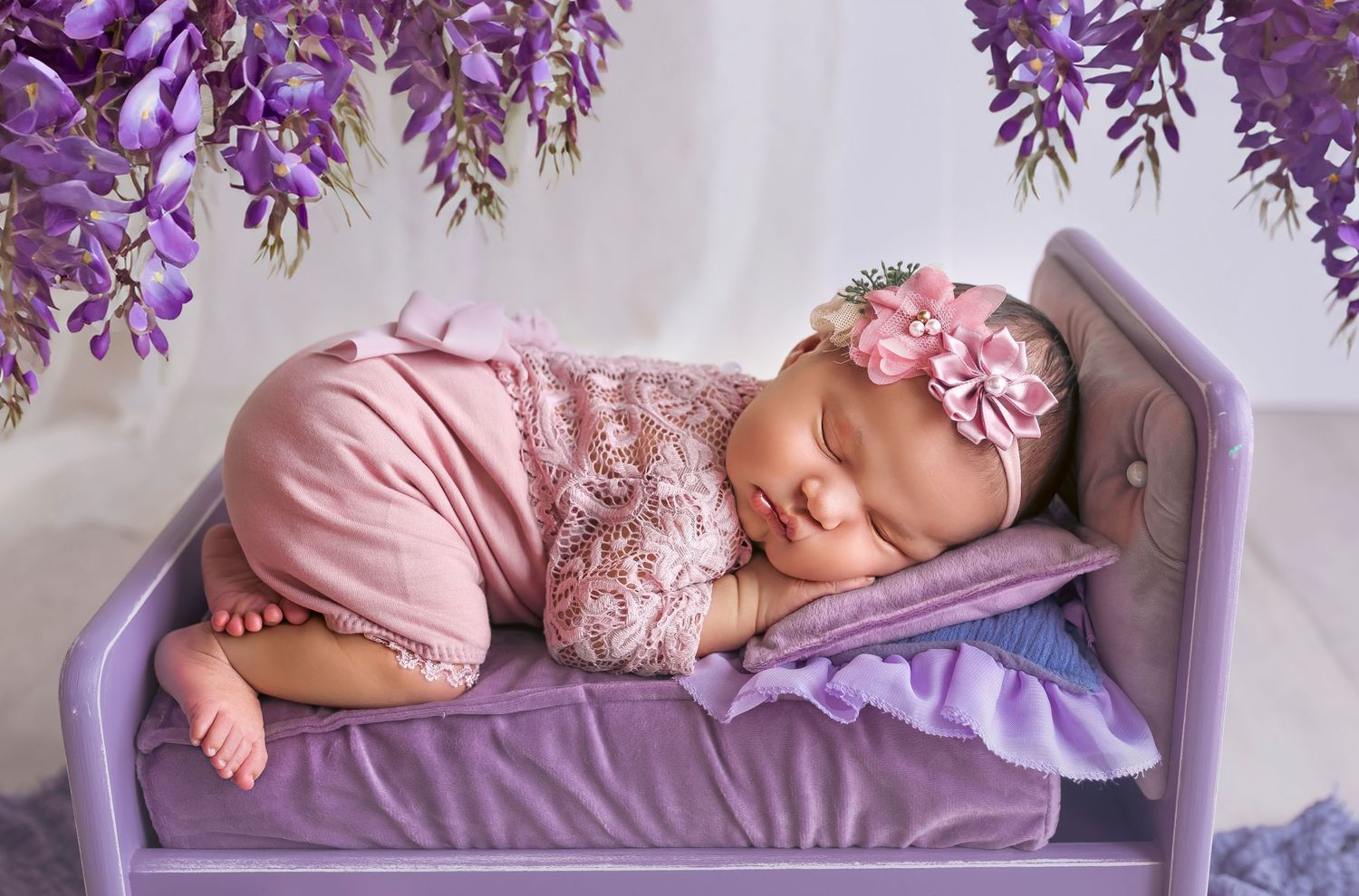 bebe recien nacida durmiendo boca abajo en una cama color purpura y flores arriba del mismo color