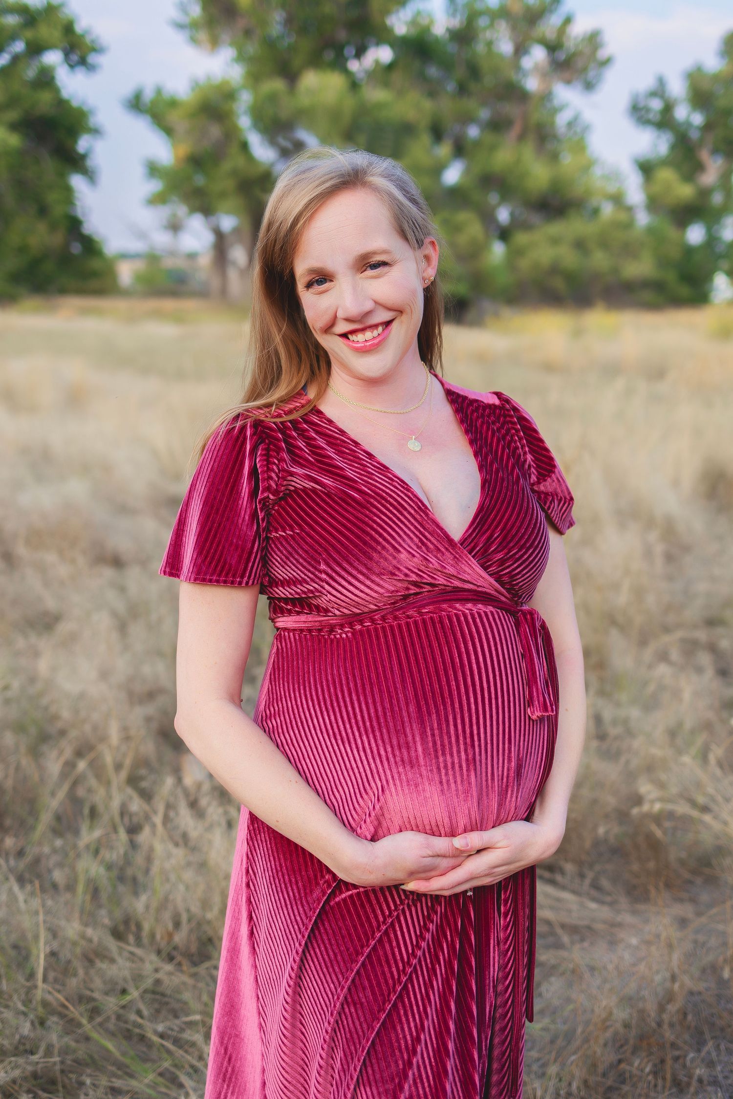 pregnant woman in a long burgundy dress.  She is outside and cradling her bump
