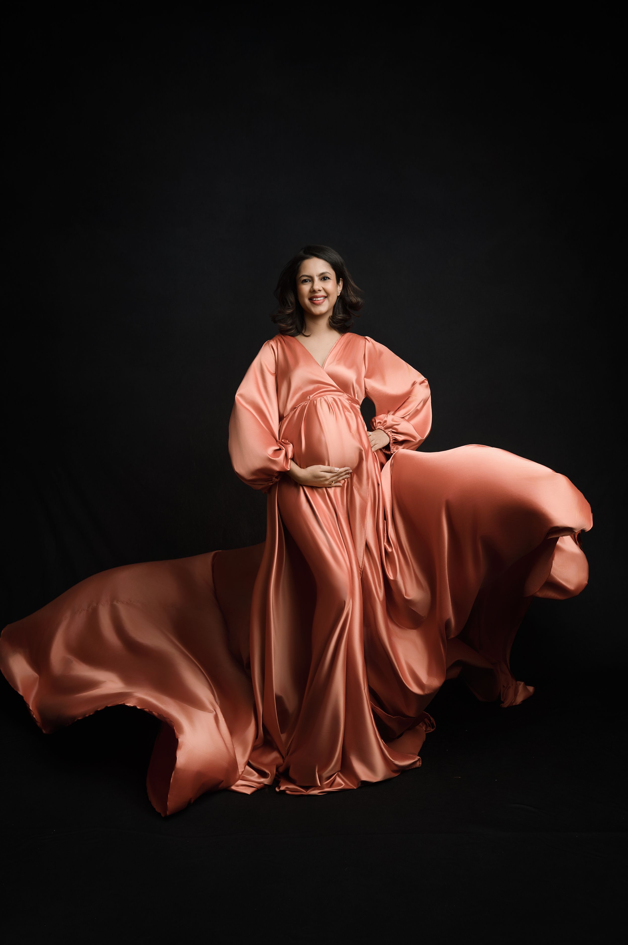 A flowing peach-colored silk dress creates elegant movement against a dark background in a fashion photography series.