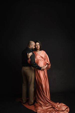 A couple embraces intimately in a dark studio setting with one person wearing a flowing peach-colored dress.
