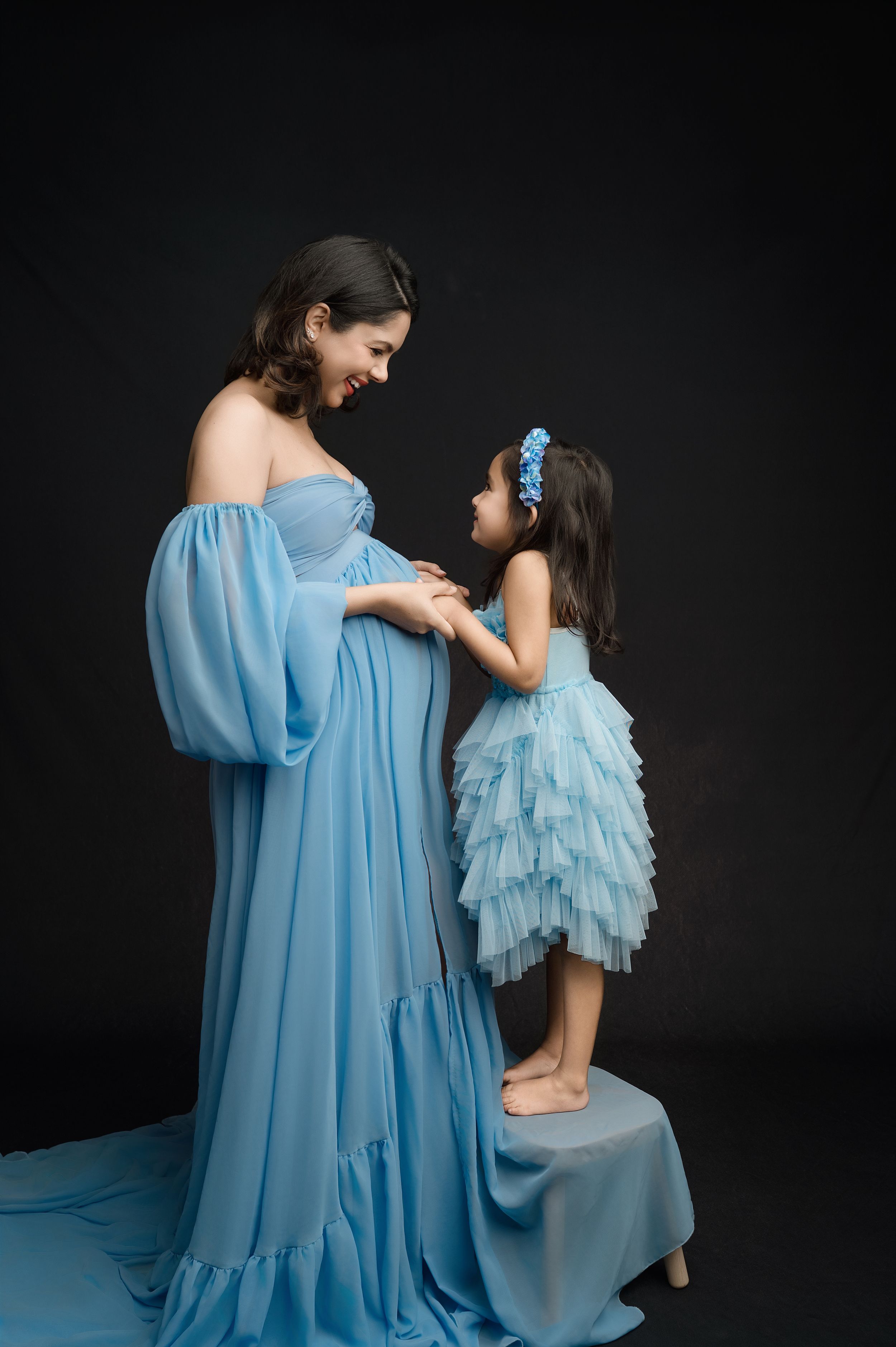 A series of intimate portraits showing a parent and child in matching light blue flowing dresses against a dark background.