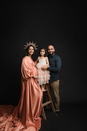 A family poses together against a dark background in coordinated outfits featuring coral and neutral tones.