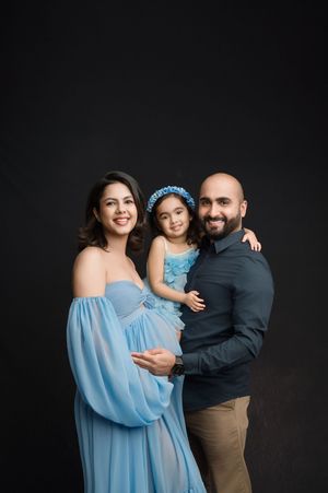 Family wearing coordinated blue and black outfits poses together against dark background in studio portrait series.