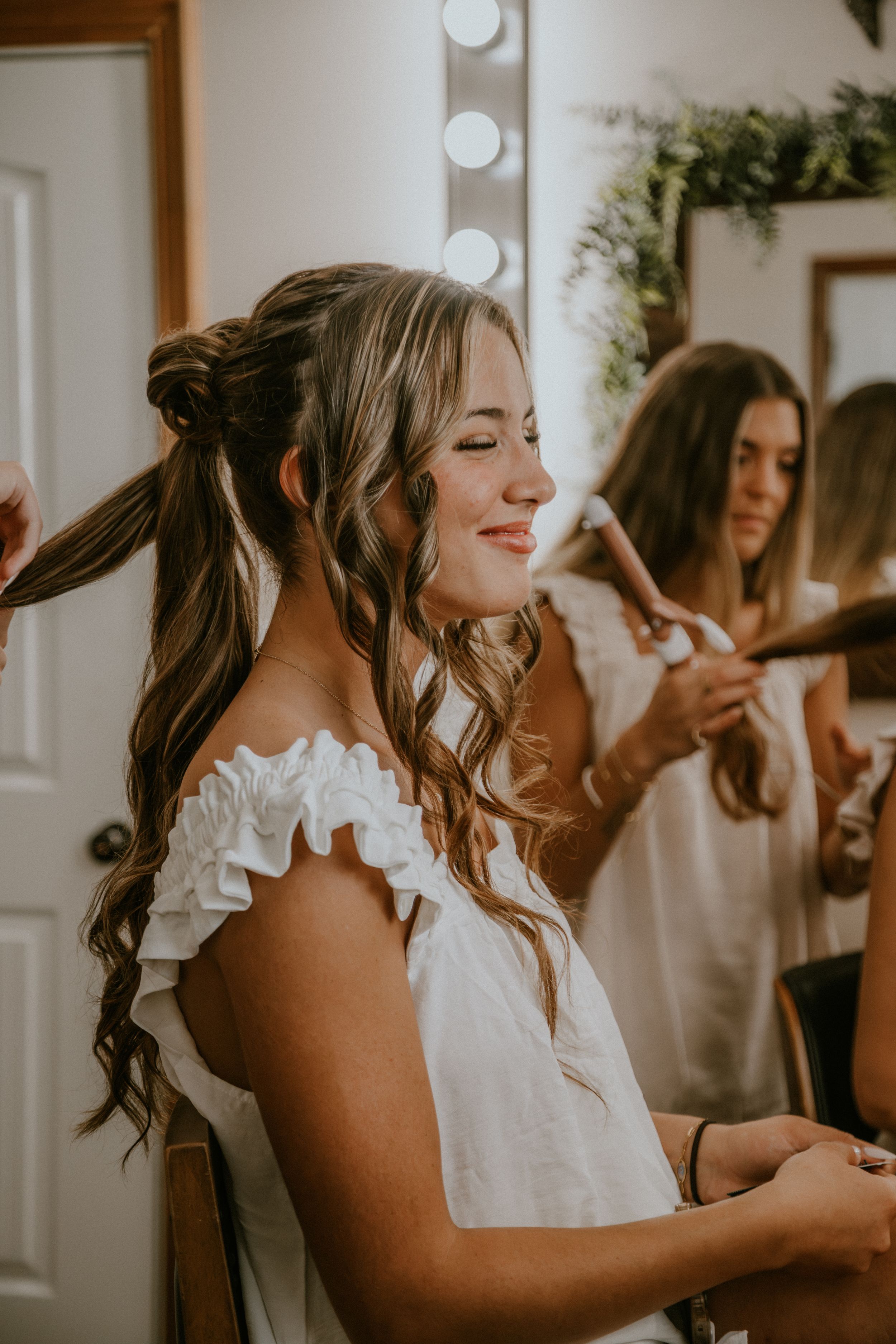 A bride and bridesmaids getting ready in a bright dressing room with white decor and natural lighting.