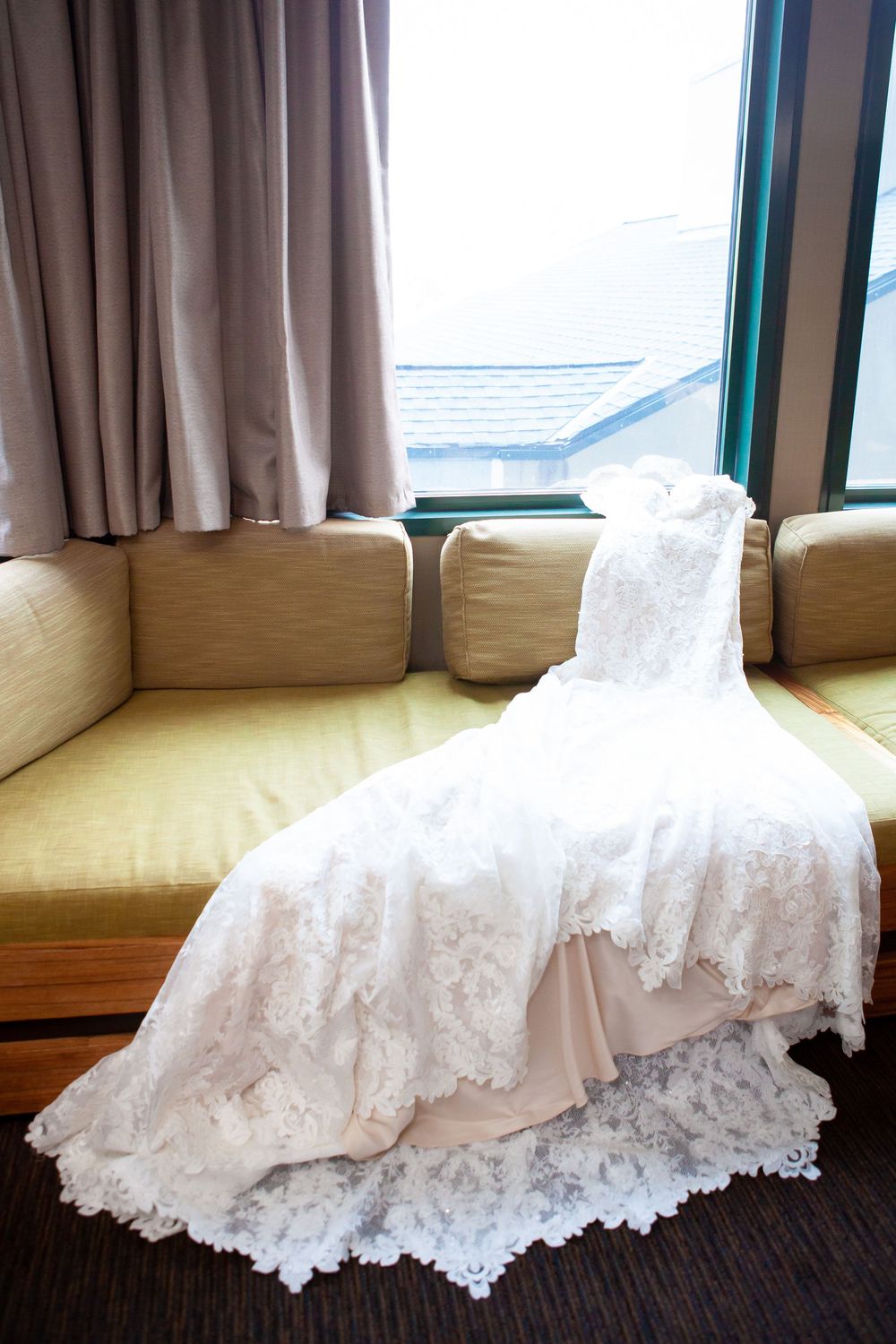 A white lace wedding dress train elegantly displayed on a beige couch.
