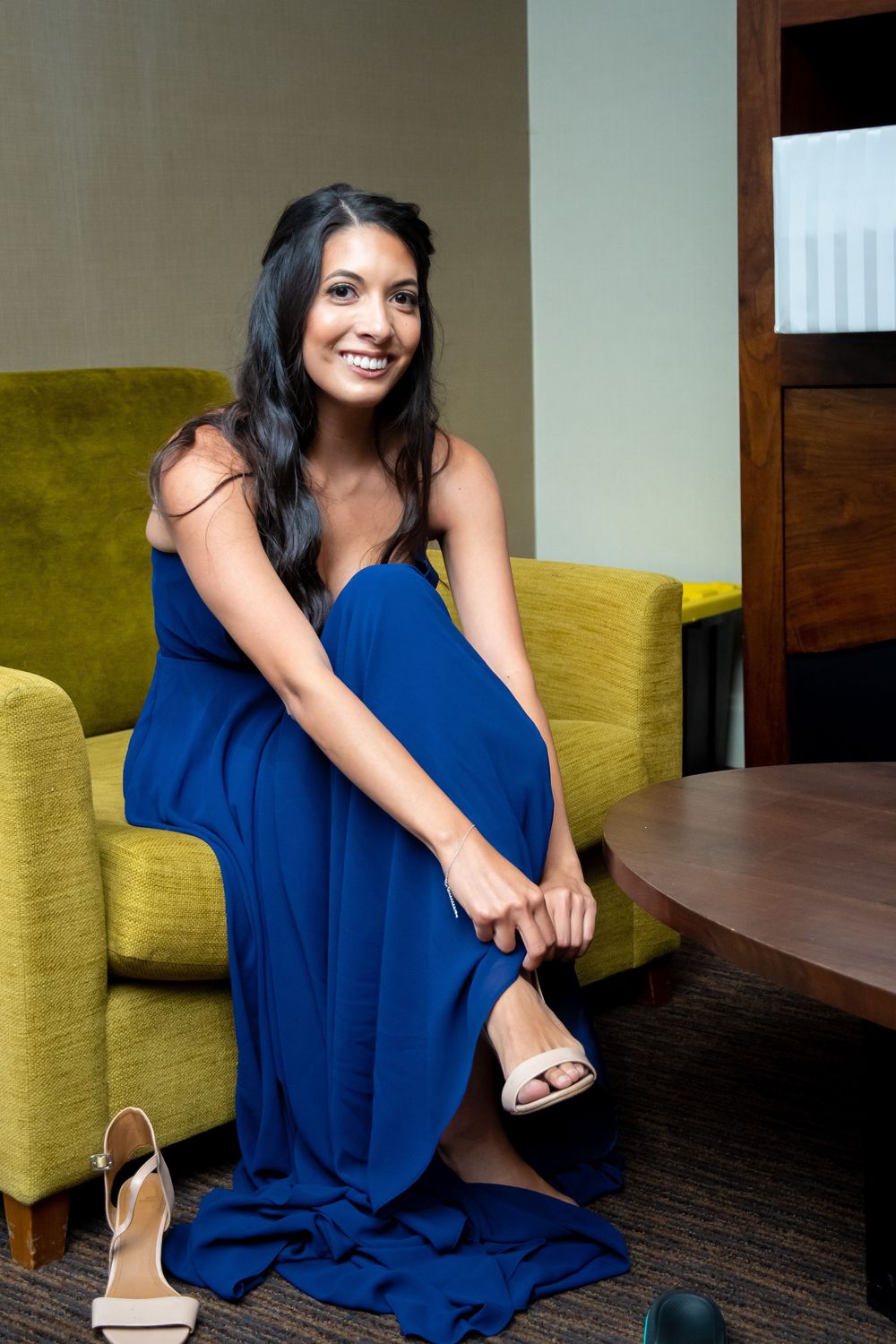 Woman in royal blue dress sits on yellow chair in modern interior setting.