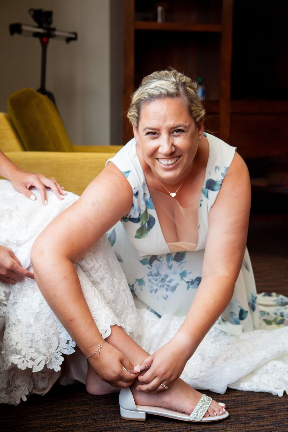 Multiple shots of a bride in a white lace dress fastening her wedding shoes on a dark wooden floor.
