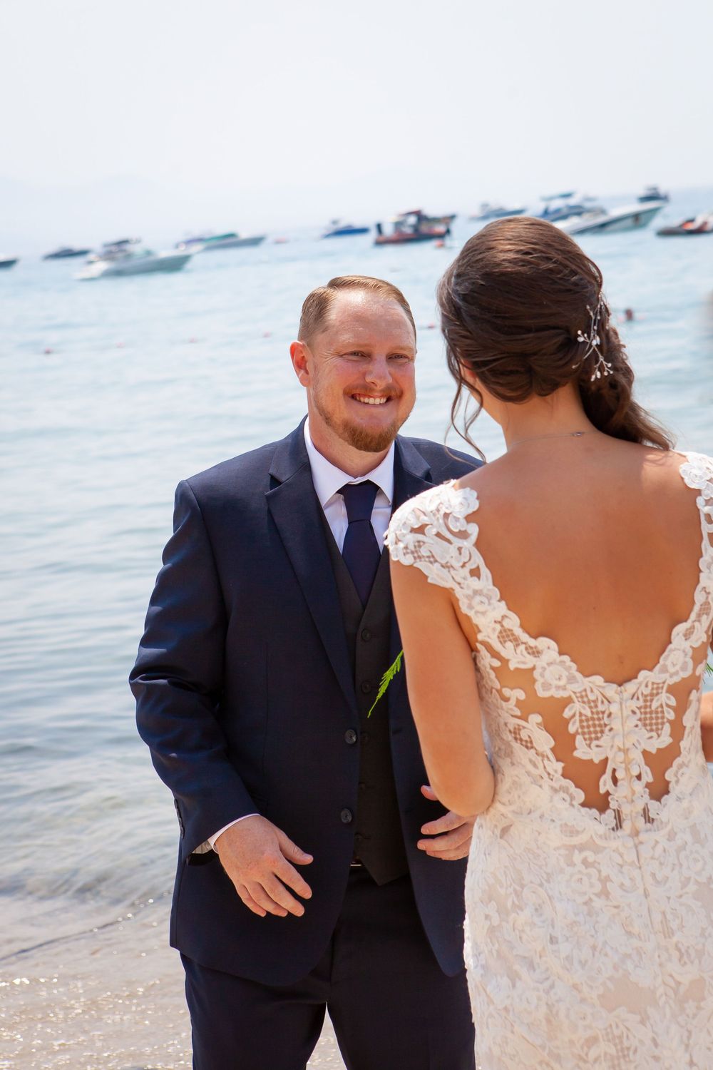A couple shares an intimate moment during their beach wedding with boats in background.