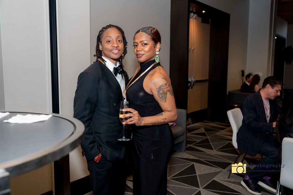 Two people in formal attire smile and pose together at an elegant event space with geometric flooring.