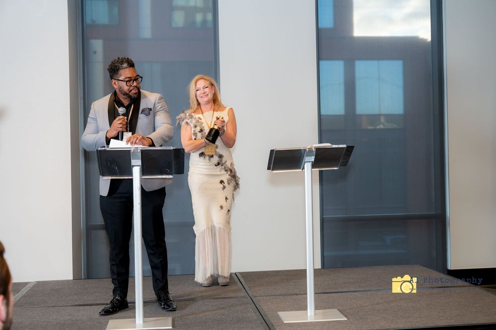 Two people stand at podiums during a presentation in a modern conference room setting.