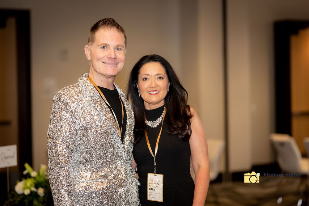 A couple poses together at a formal event, with one person wearing a sparkly silver dress and the other in black attire.