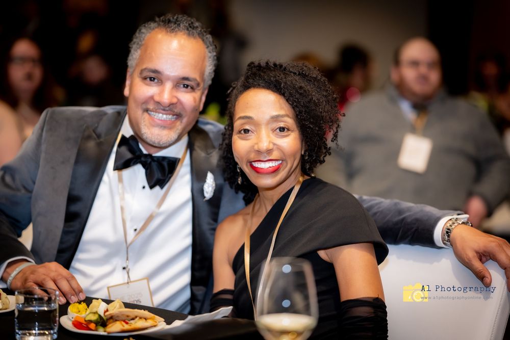 Attendees in formal attire enjoying a corporate gala dinner event with bright smiles and elegant table settings.