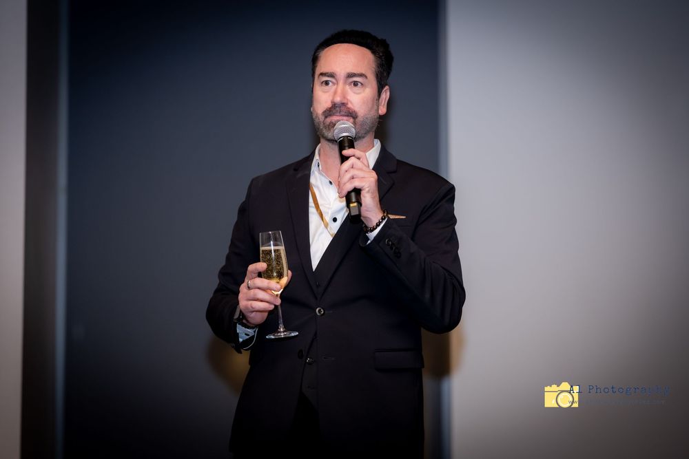 A person in a dark suit holds a glass of wine against a black background in a series of progressive shots.