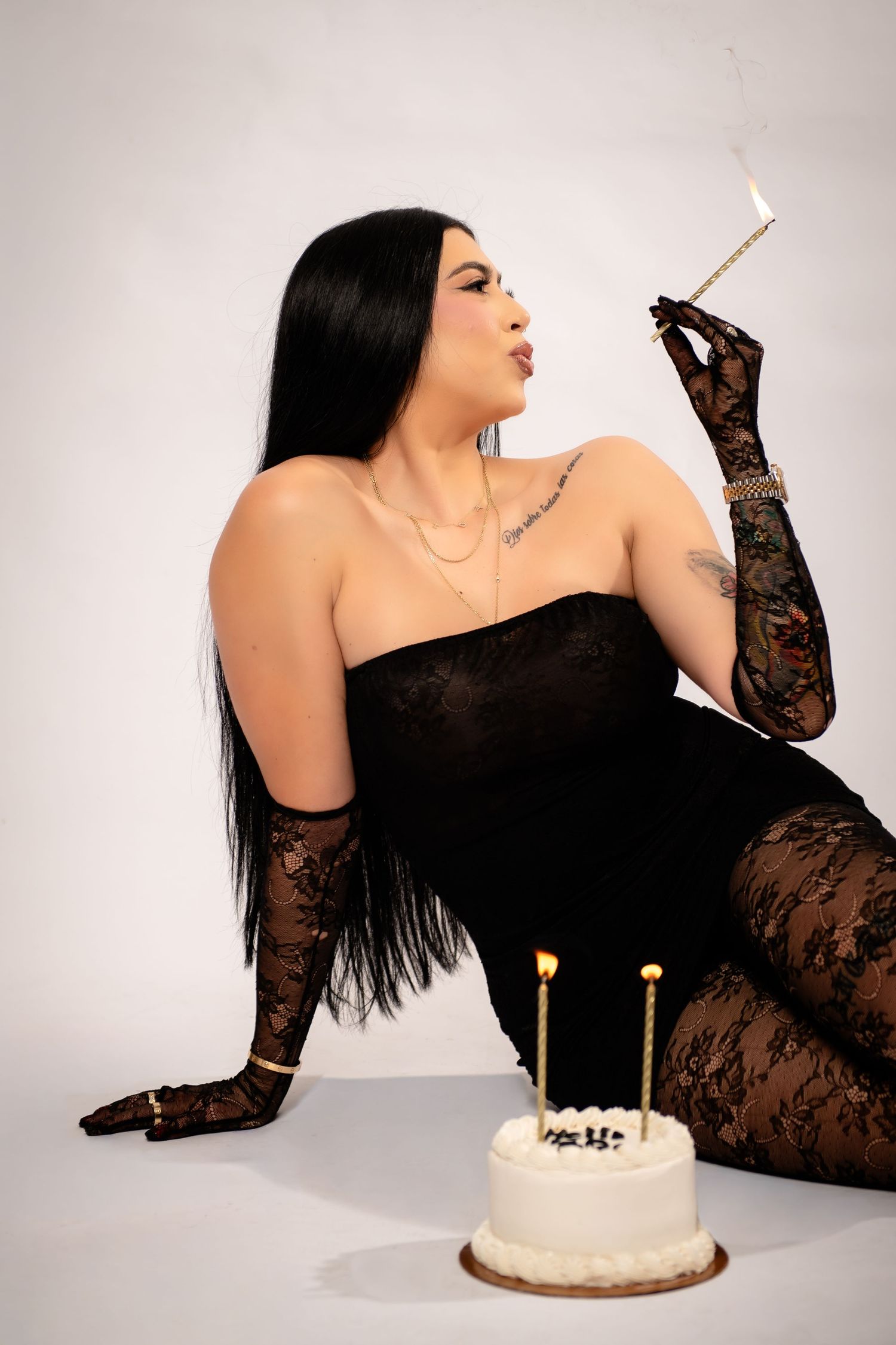 Glamorous portrait with black lace gloves, strapless dress, birthday cake and dramatic pose against white backdrop.