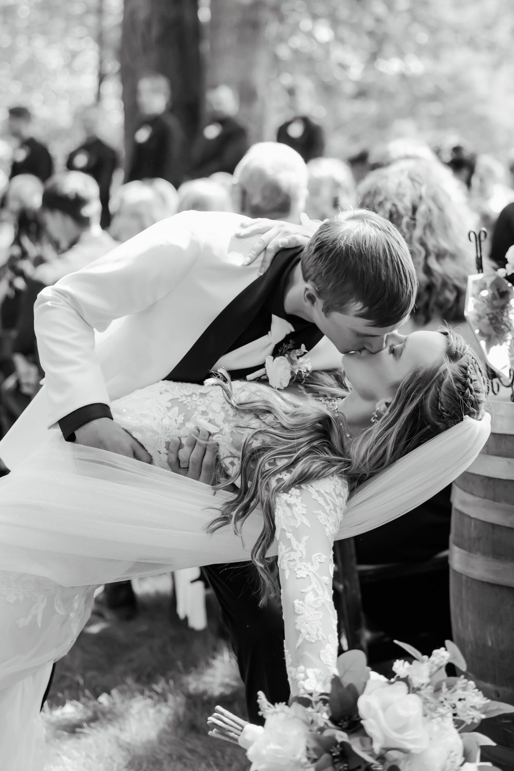 A dramatic dip kiss captured in black and white during an outdoor wedding celebration.