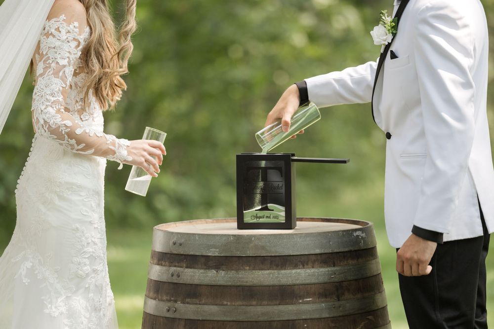 A couple performs a unity ceremony ritual using a wooden barrel and black lantern outdoors.