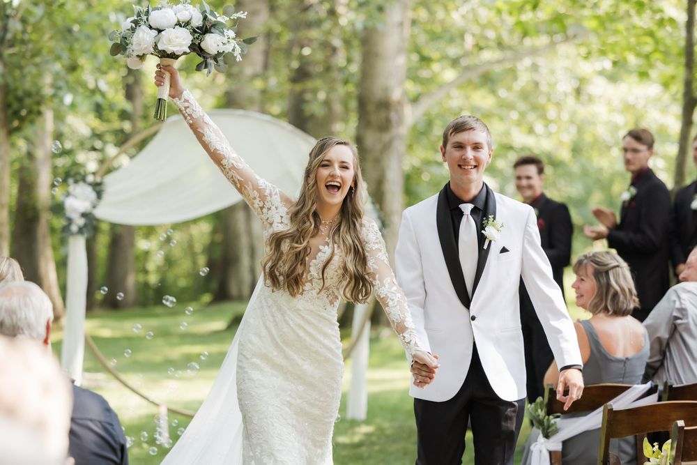 Wedding party in burgundy dresses and white tuxedos poses outdoors.