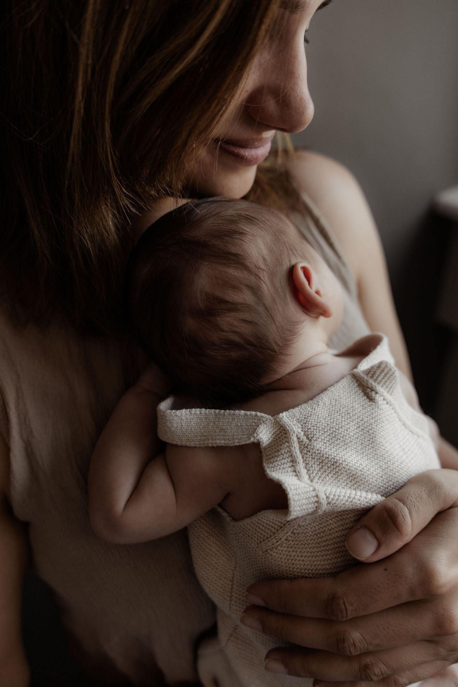 A tender moment captured in warm tones as a parent cradles and embraces their newborn baby in soft natural light.