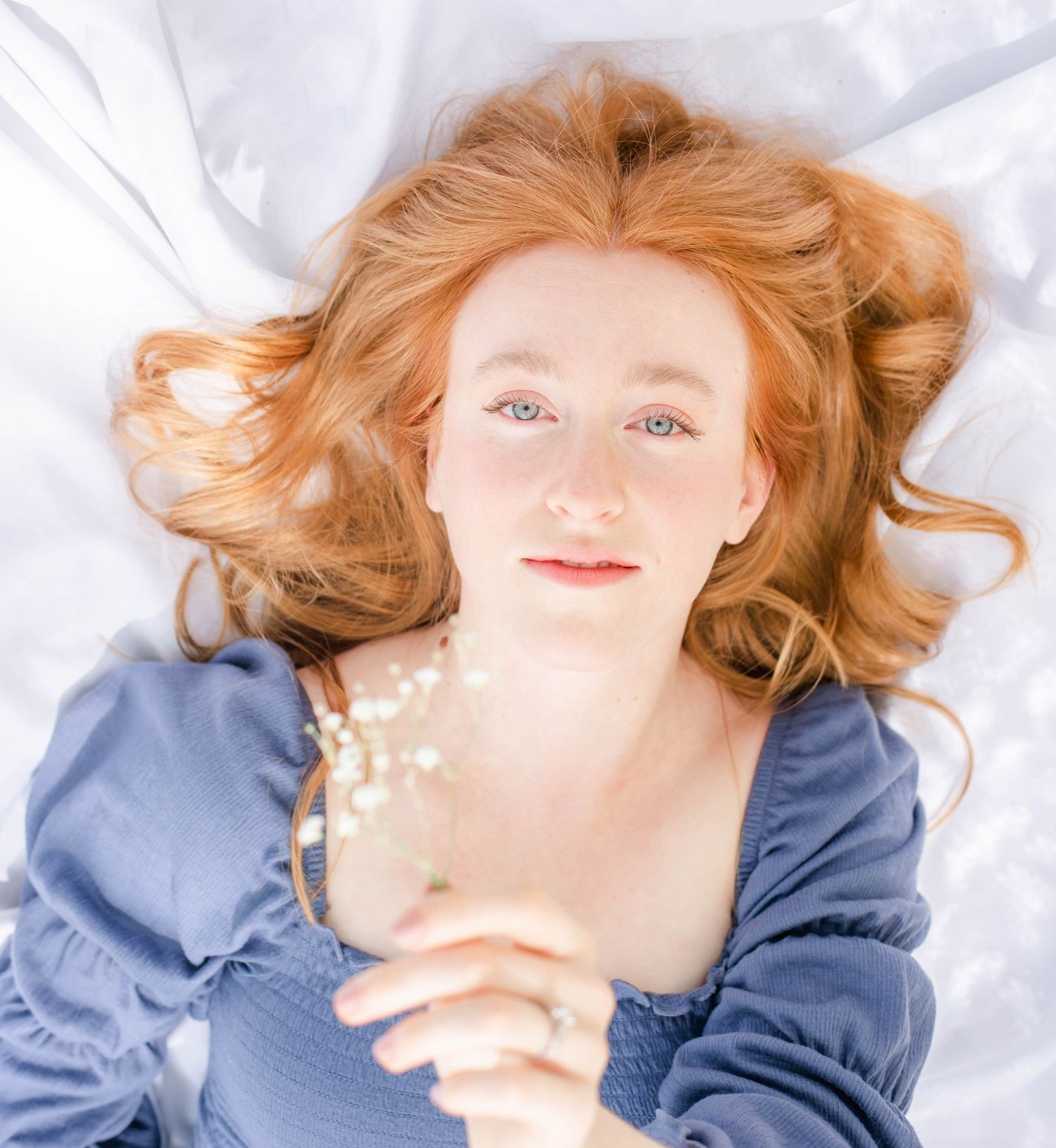 Person with red hair lying on white fabric wearing blue clothing in a sequence of artistic portrait poses.