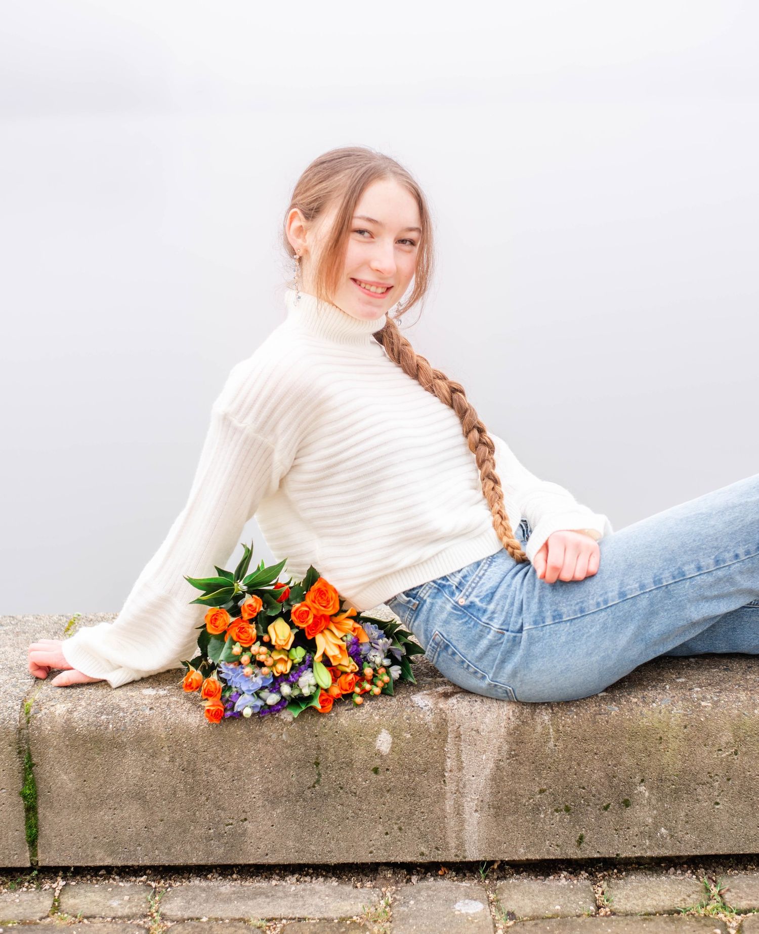A person in a white sweater lying on concrete with colorful flowers beside them.