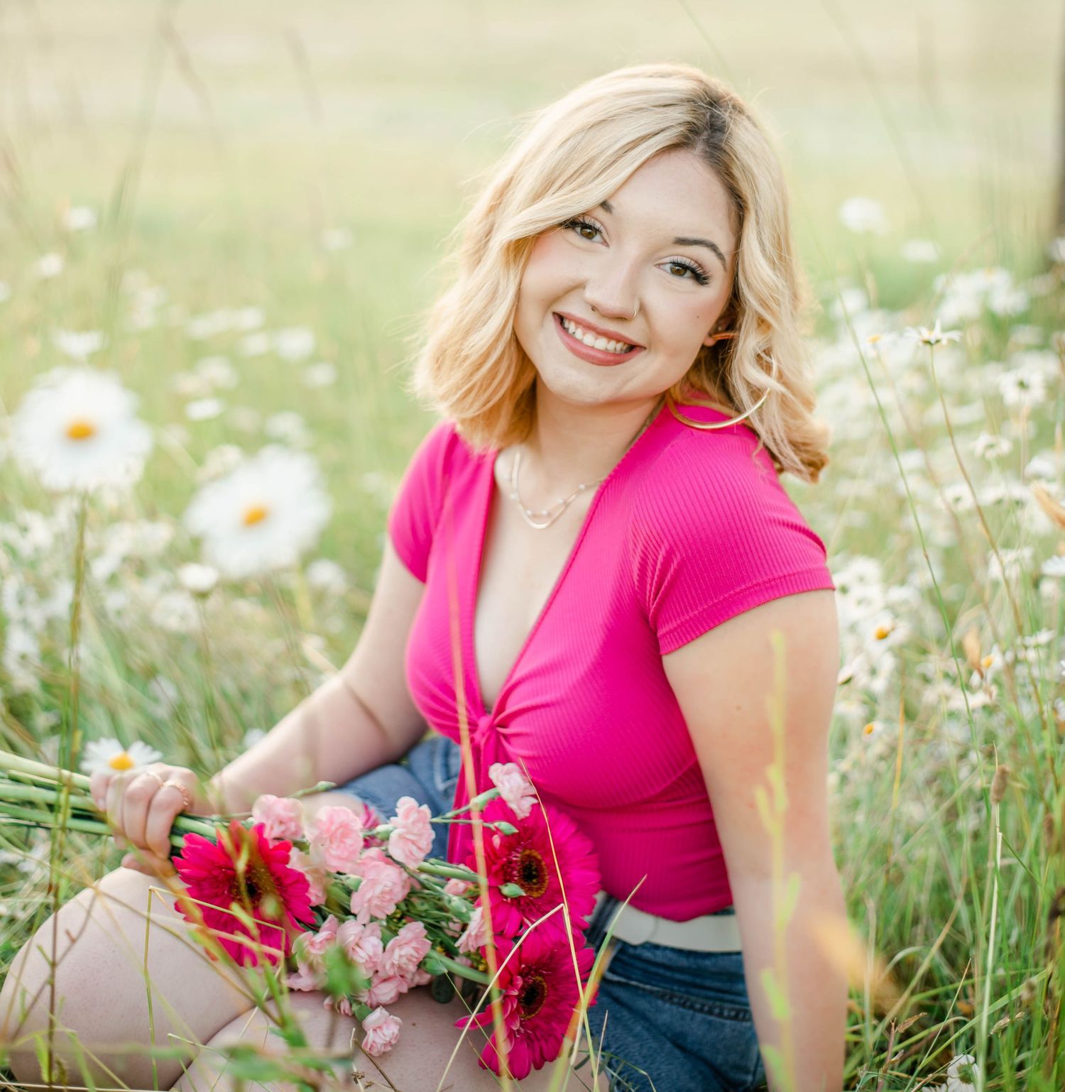 Woman in pink top sitting in field of white daisies during summer photo session.