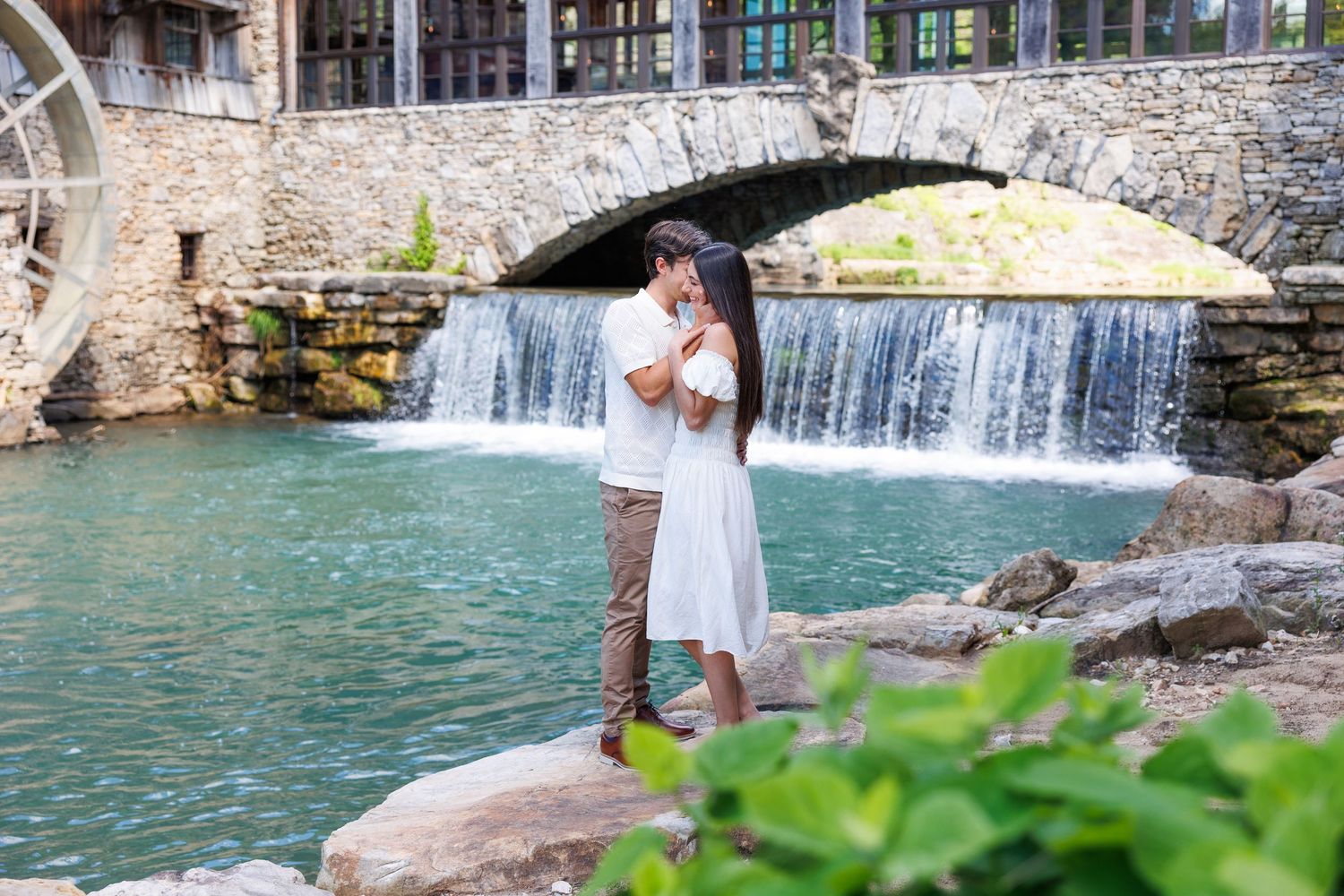 A white dress against a stone bridge with cascading waterfall and turquoise water at a scenic outdoor location.