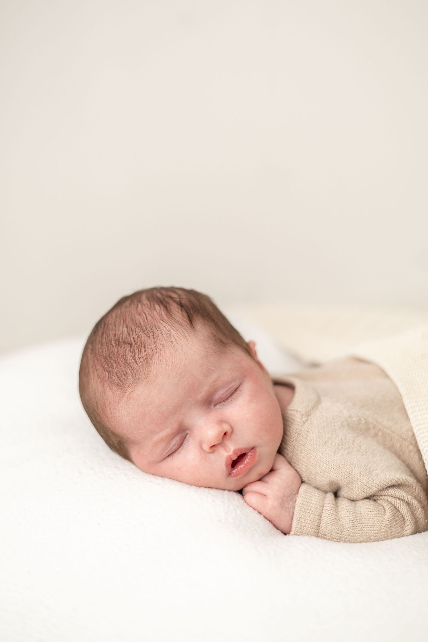 A sleeping newborn baby wrapped in beige fabric lies peacefully on a white background during Newborn Photoshoot Nottingham