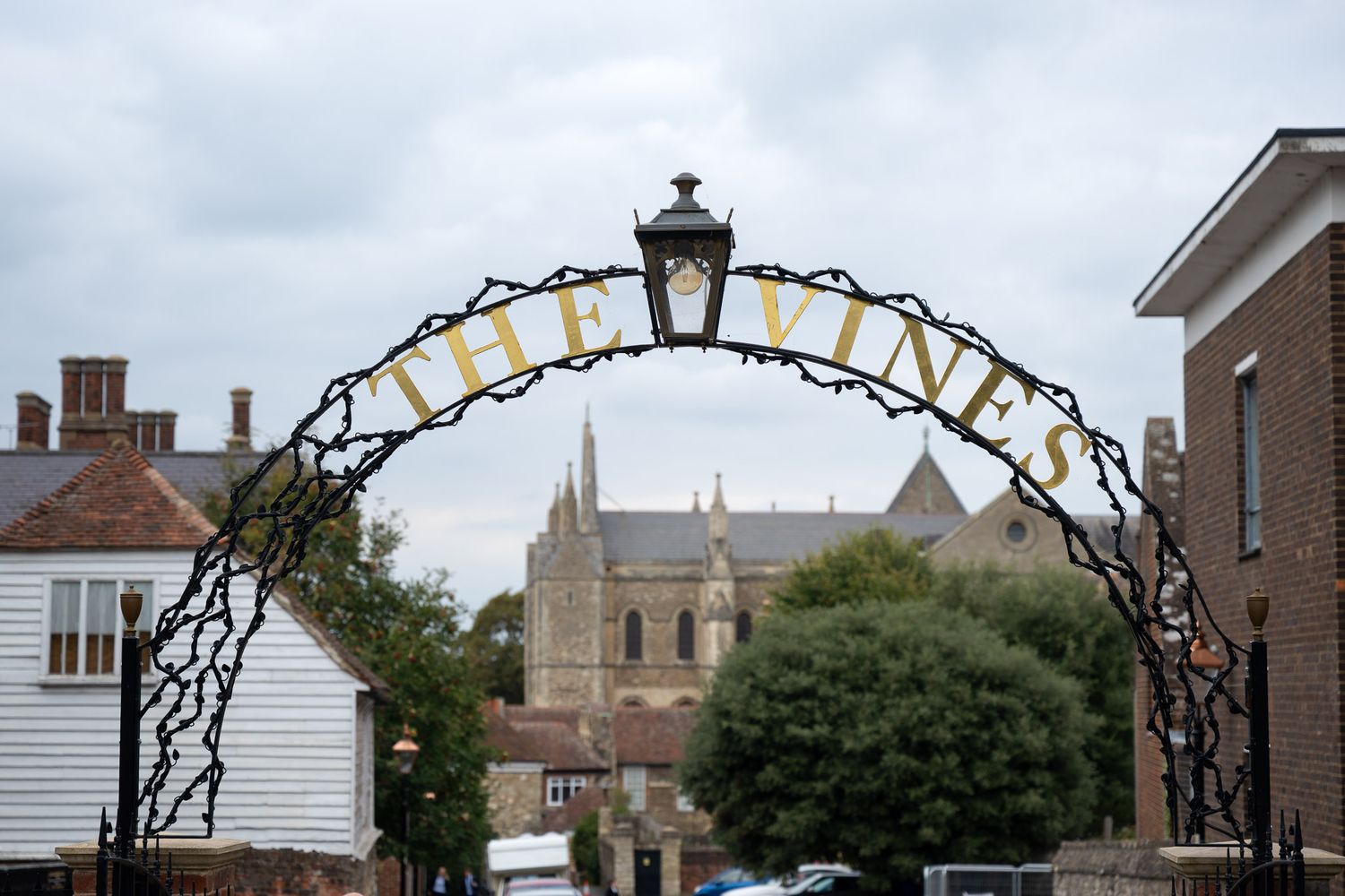 A panoramic view of historic brick buildings and trees along a city street with an ornate lamp post in the foreground.