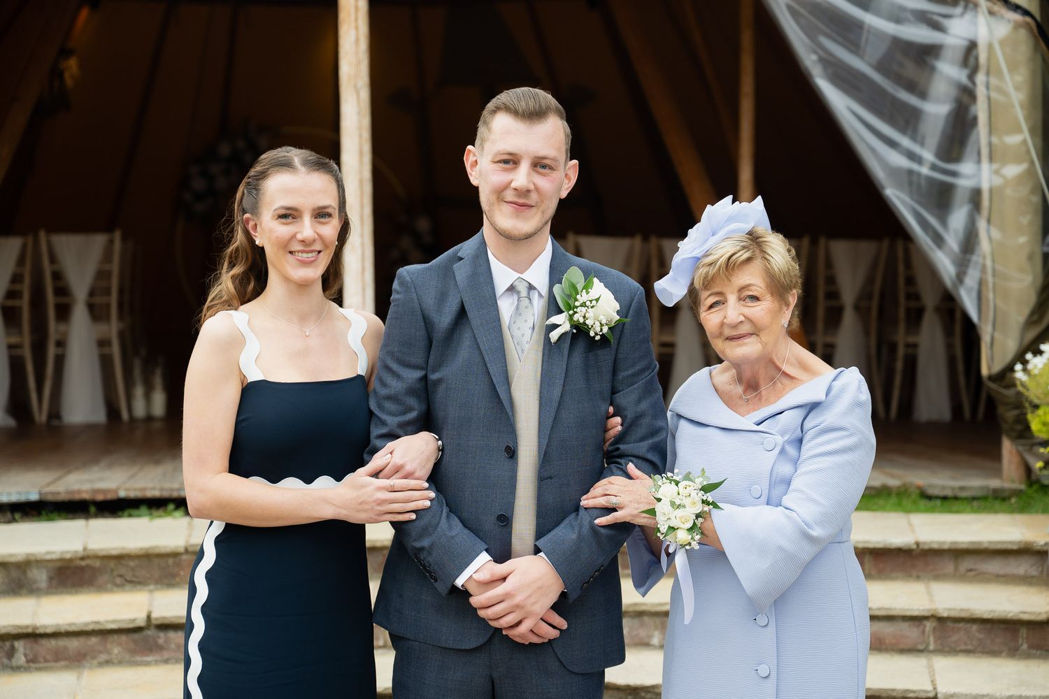 Wedding party poses together in formal attire with bouquets at outdoor venue.