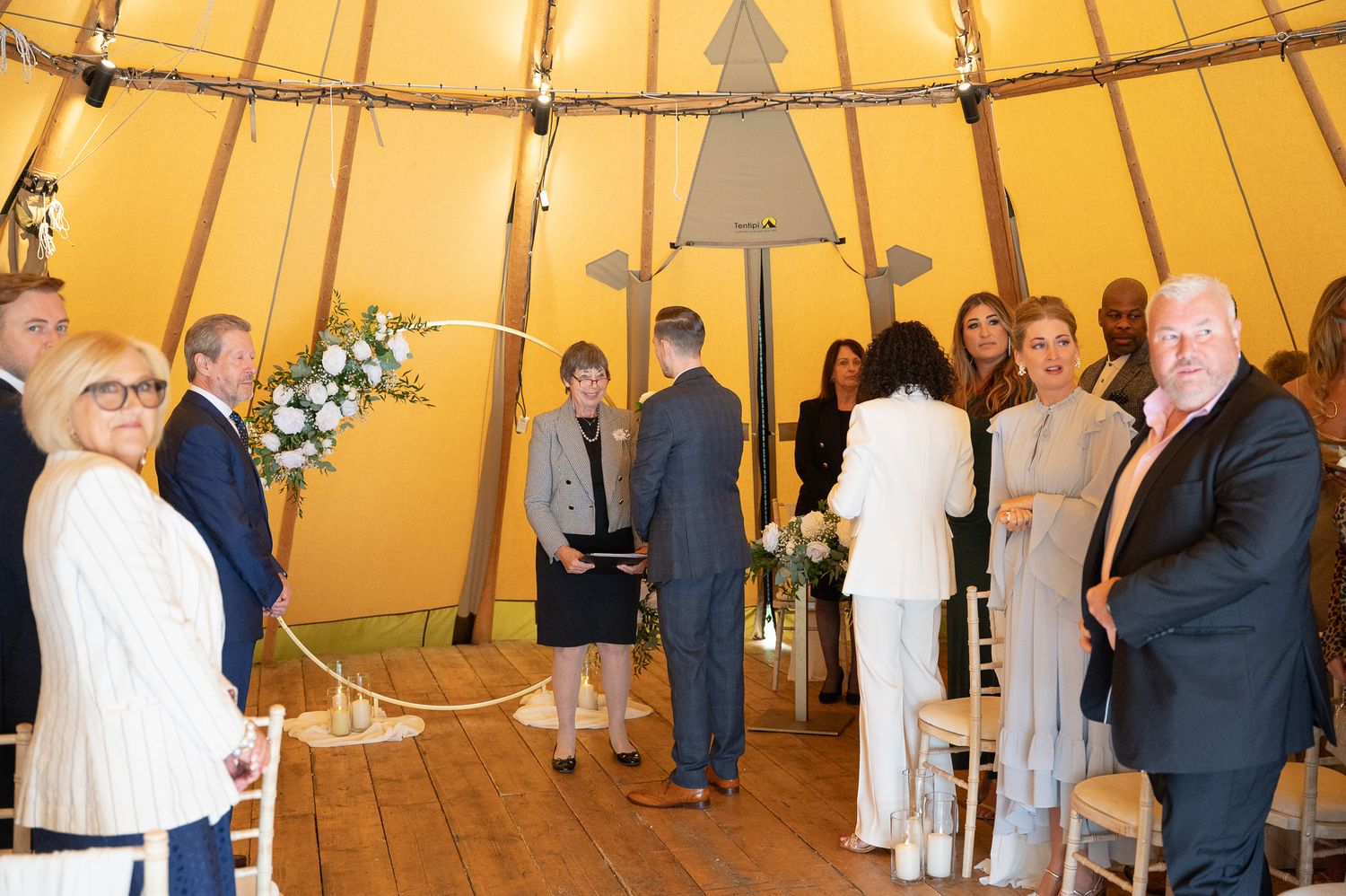 A panoramic view of a wedding reception inside a large tipi tent with guests mingling under warm lighting.