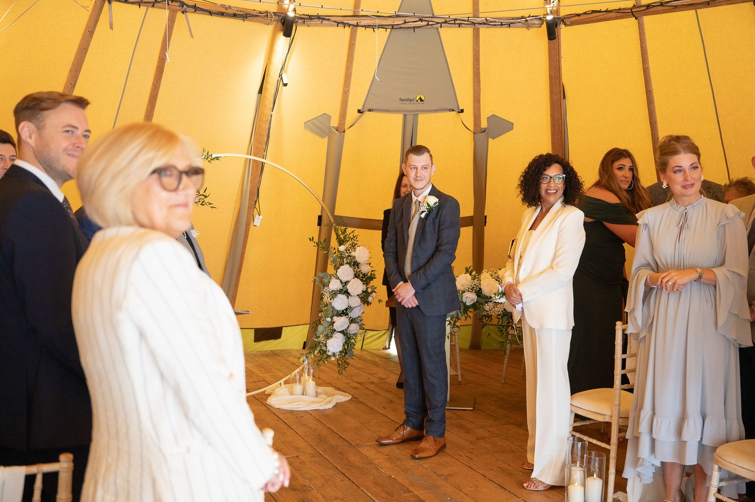 People gather inside a warm-lit tipi-style tent for what appears to be a wedding ceremony or special event.