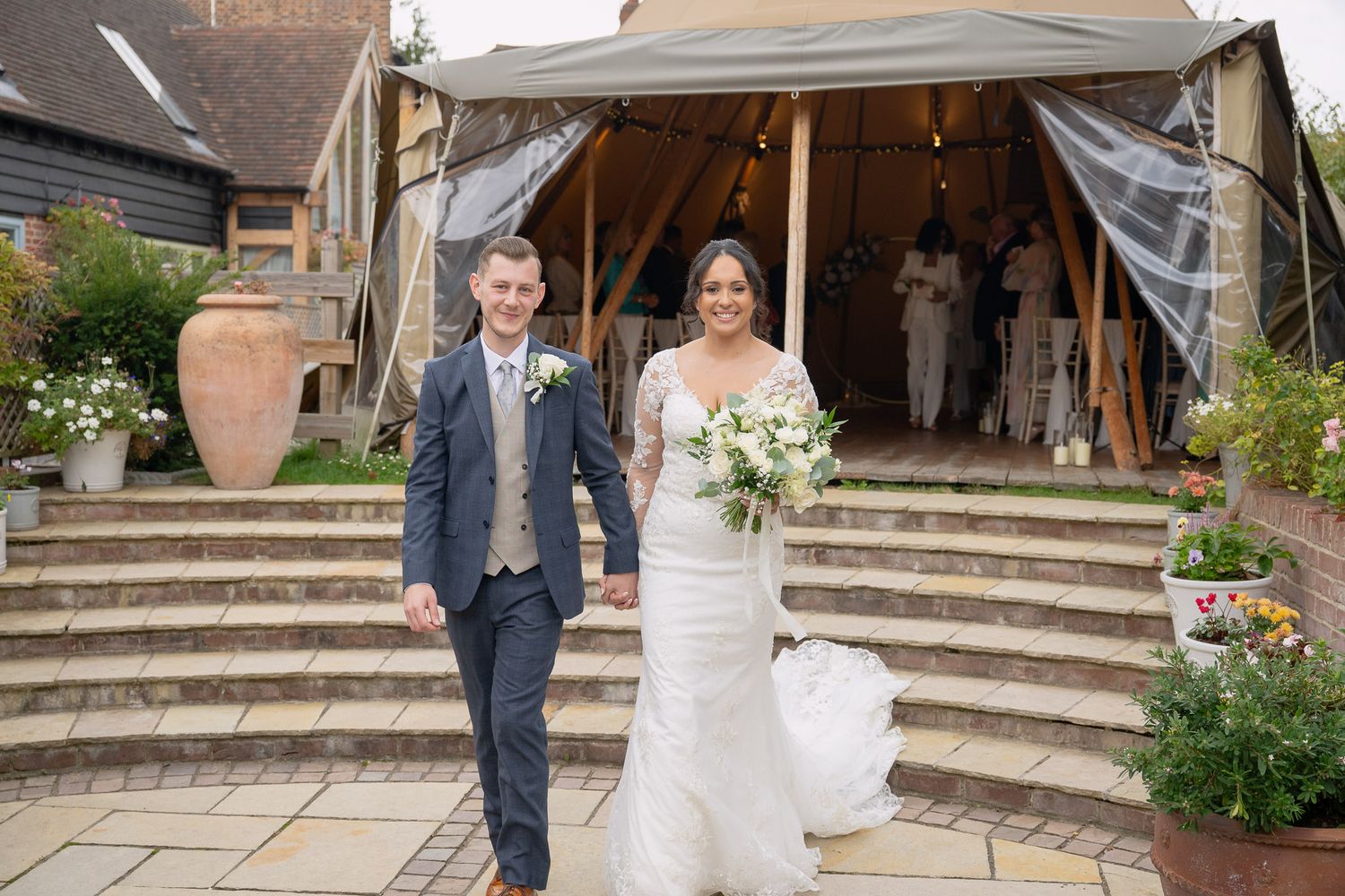 A couple in wedding attire poses together on stone steps at a rustic venue.