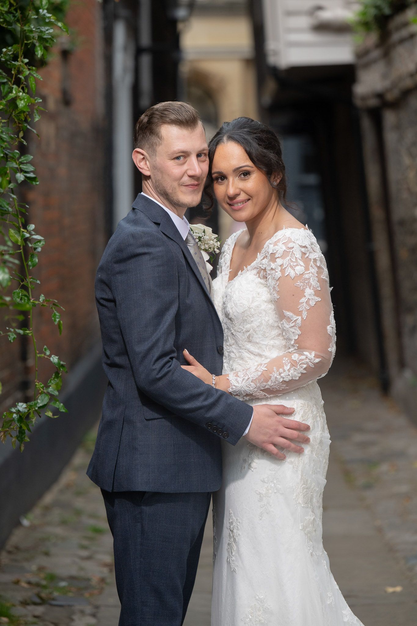A romantic wedding couple shares intimate moments in a brick-lined alleyway while wearing elegant formal attire.