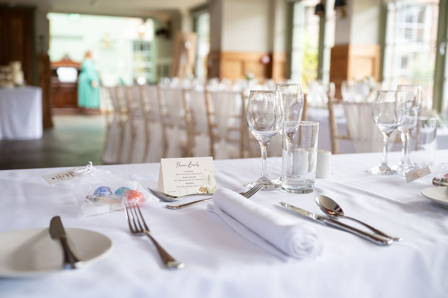 Elegant table settings with white linens, wine glasses and silverware in a bright dining room.