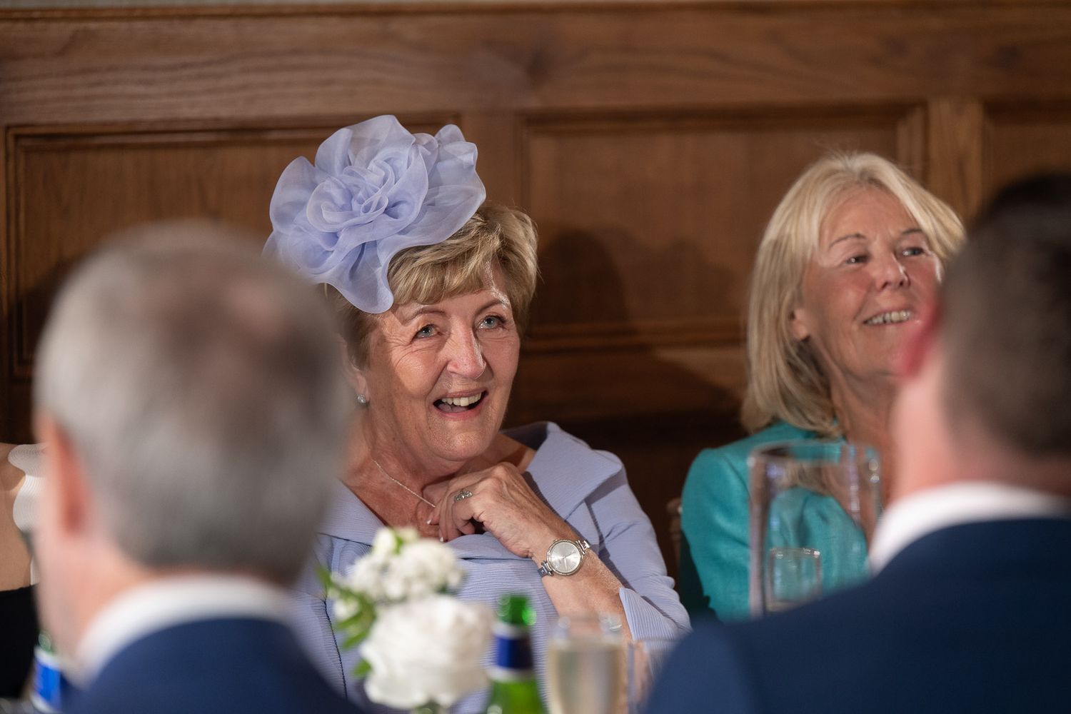 Wedding guests share laughter and conversation during a reception at a rustic wooden venue.