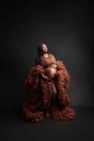 Artistic maternity portrait featuring an elegant brown tulle robe against a dark studio backdrop.