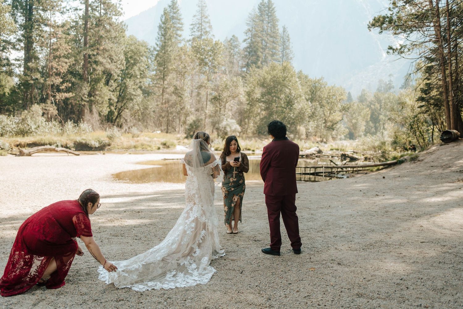 Wedding party arranges bride's lace train during outdoor elopement ceremony in Yosemite Valley.