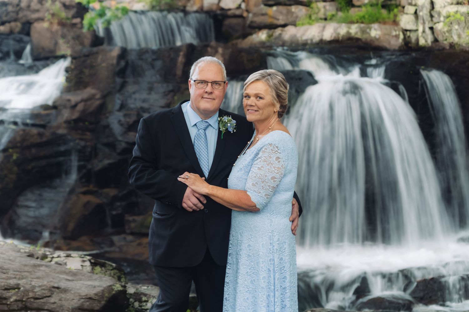 A photograph of an older couple standing by a waterfall