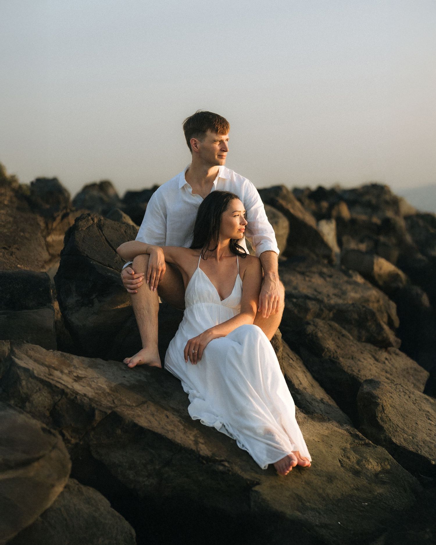 Bride and groom sitting on coastal rocks during golden hour wedding portrait session
