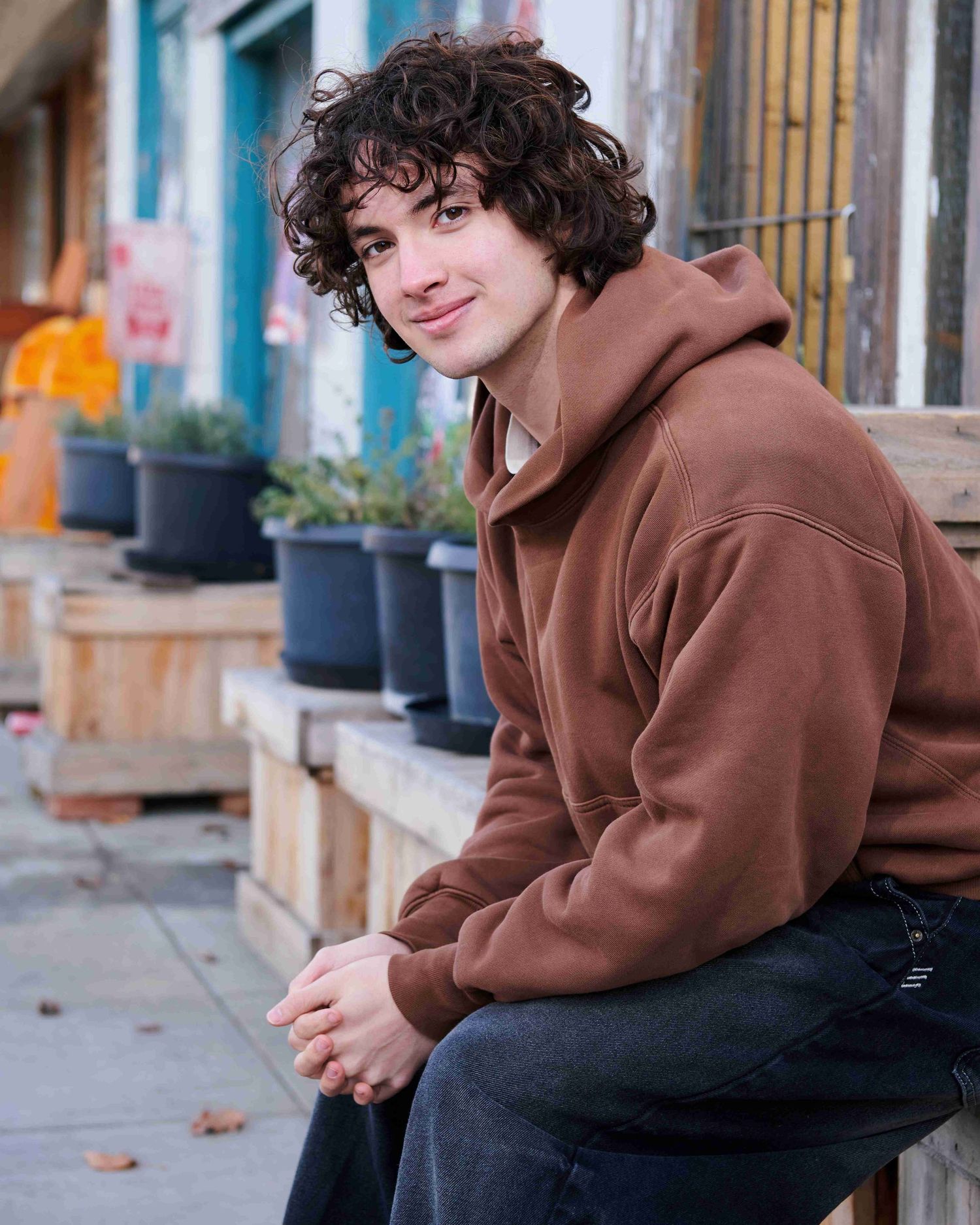 Marshall's high school senior photo sitting downtown Okanogan, WA while wearing a brown sweatshirt and smiling.