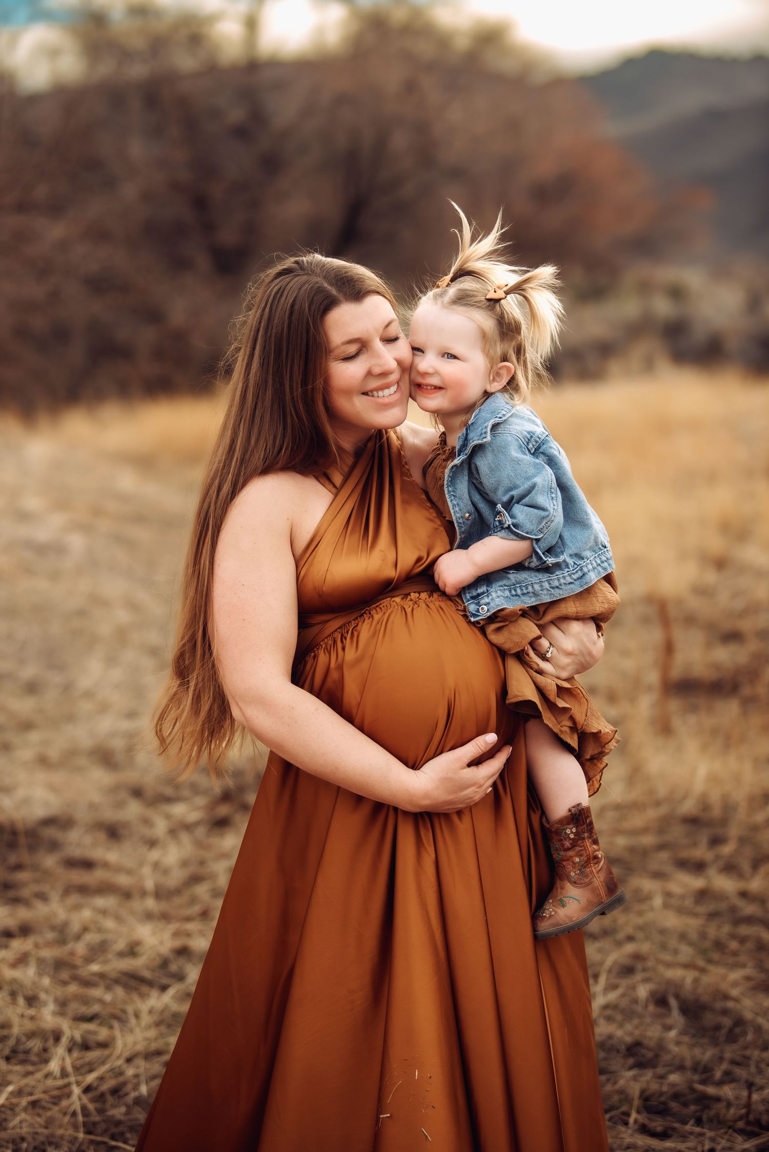 Mother and child in matching brown dresses share tender moments in a golden autumn field at sunset.