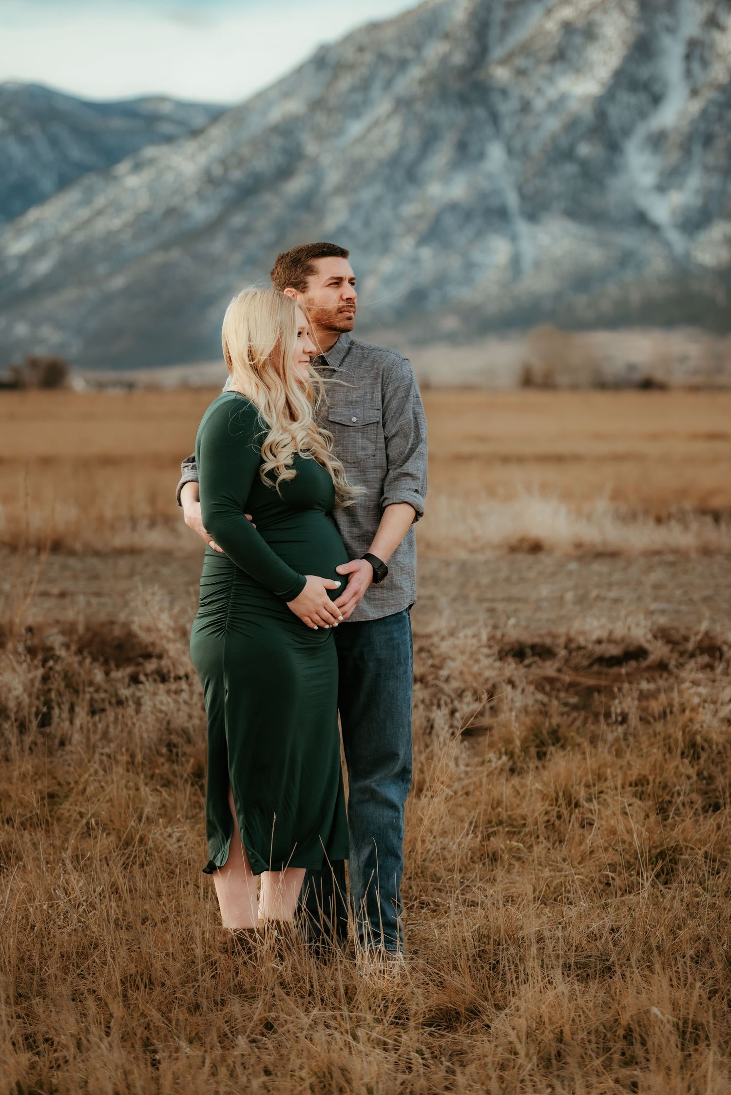 A couple embraces in a field with dramatic mountain landscape in the background.