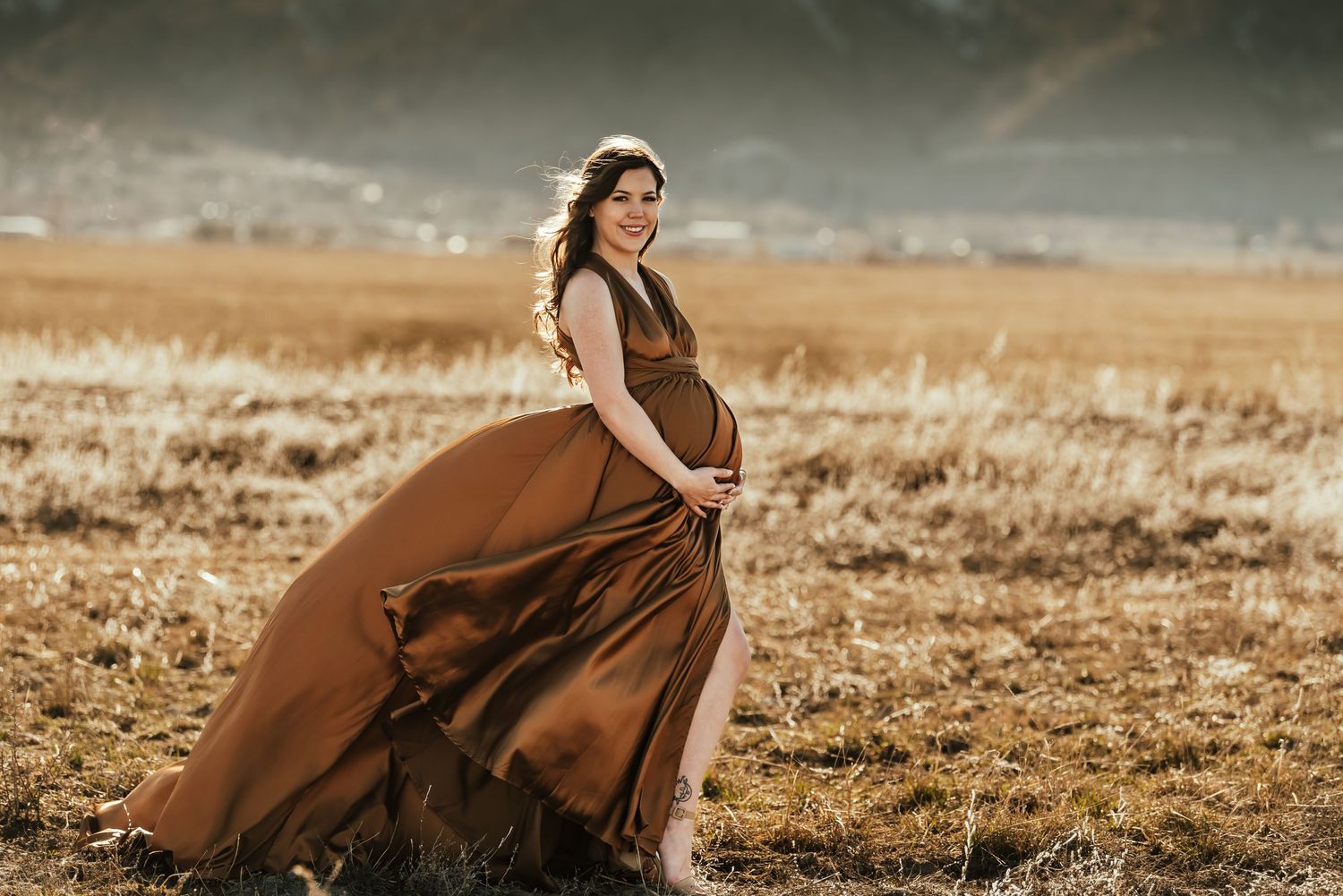 A flowing brown dress captures movement in a golden field with mountains in background.