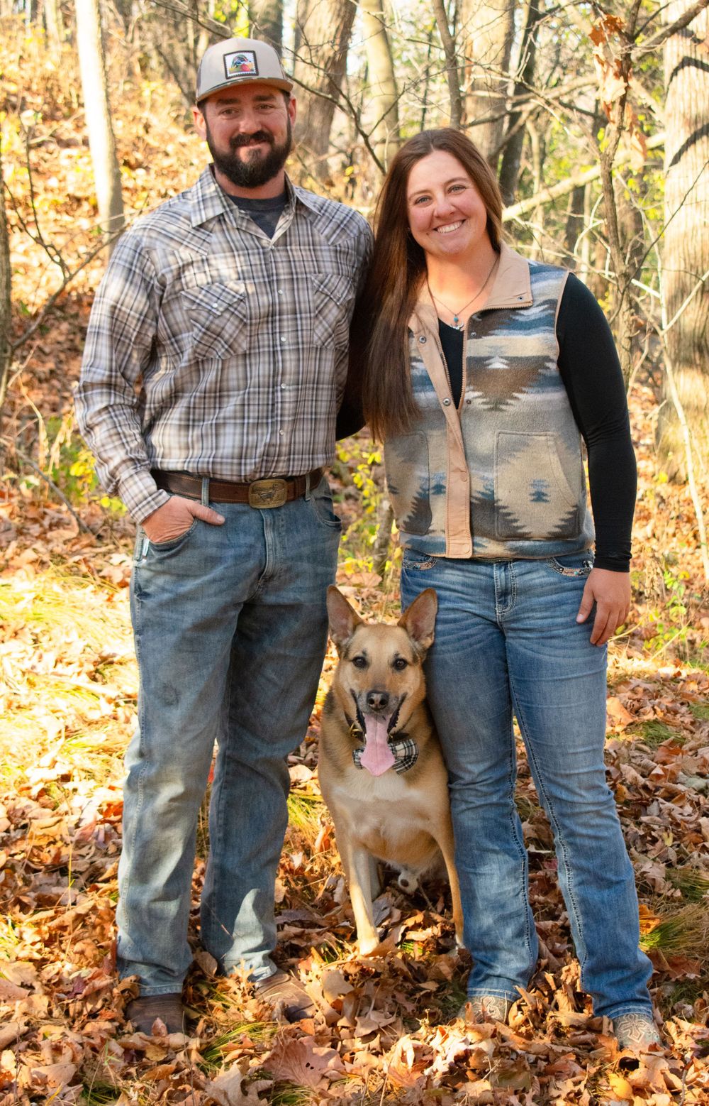 Boyfriend and girlfriend with their dog in the middle of them, all three smiling.